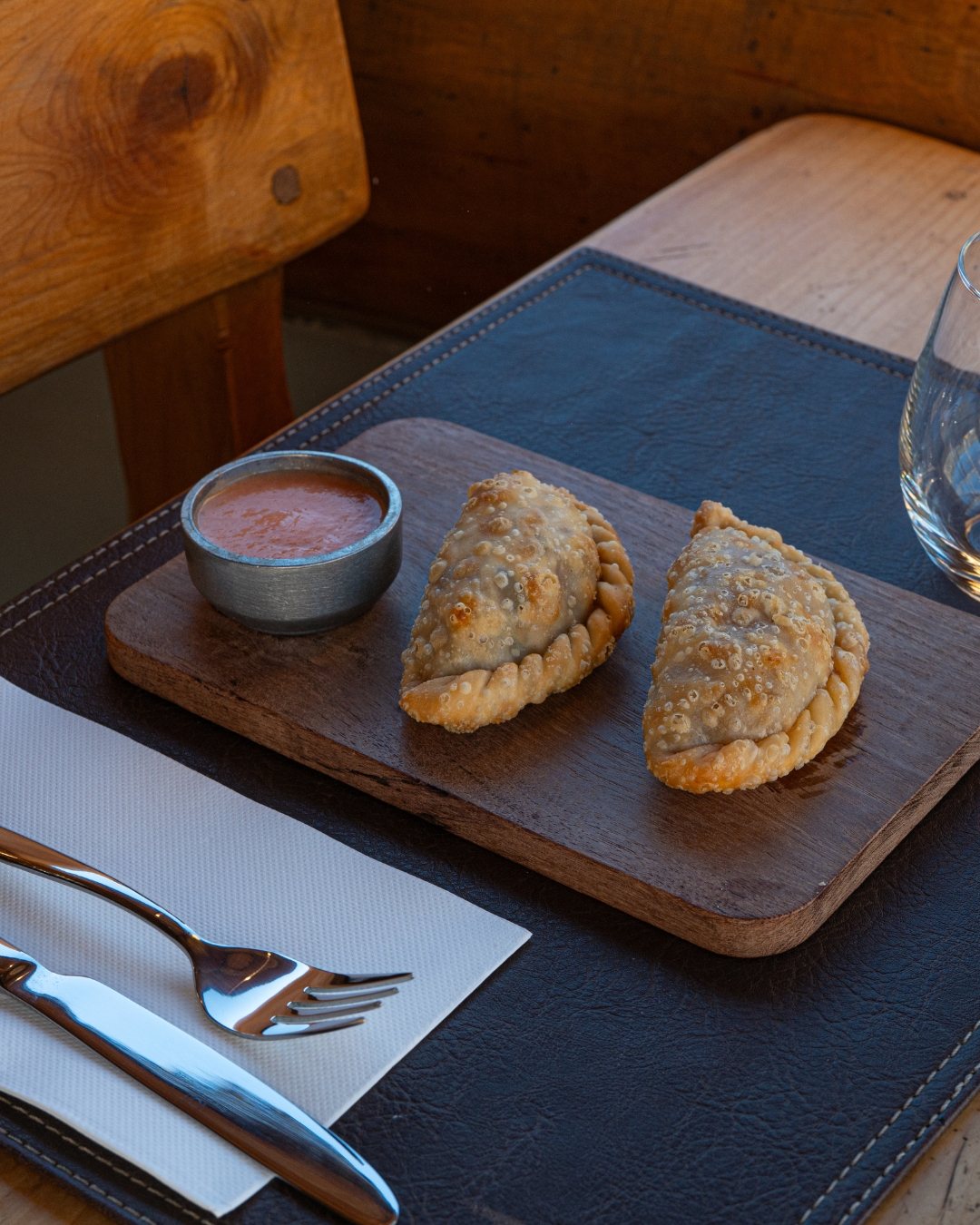 Dos empanadas fritas sobre tabla de madera con salsa