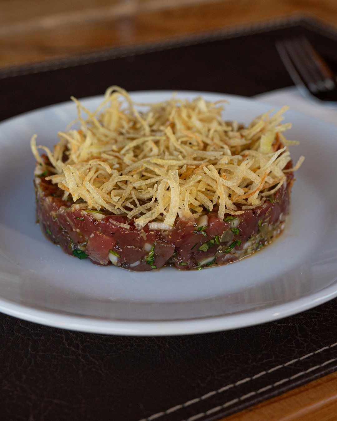 Tartar de guanaco con papas payán sobre plato blanco